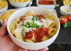 a person holding a bowl of pasta with sauce and parmesan cheese