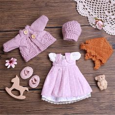 doll clothes and accessories laid out on a wooden surface with crocheted doily