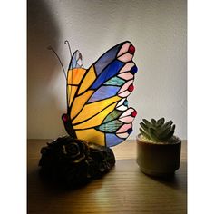 a colorful butterfly lamp sitting on top of a table next to a potted plant