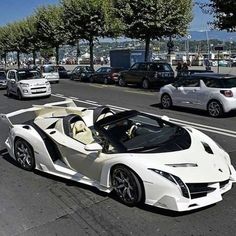 a white sports car driving down a street next to parked cars on the side of the road