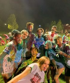 a group of people covered in colored paint posing for a photo on the grass at night