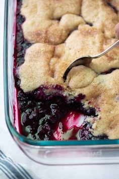 a spoon is being used to scoop blueberry cobbler into the casserole