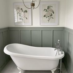 a white bath tub sitting in a bathroom next to two framed pictures on the wall