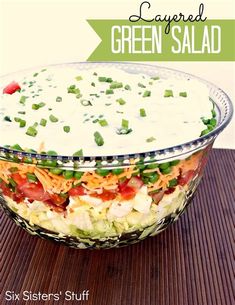 layered green salad in a glass bowl on a wooden table with the title text below it