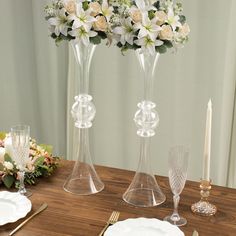 two tall vases with white flowers are sitting on a table next to plates and silverware