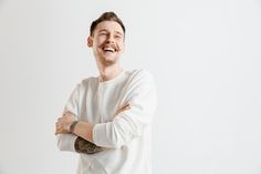 a man with his arms crossed standing in front of a white wall and smiling at the camera