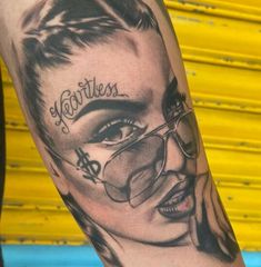 a woman's face with glasses and the word fearless tattooed on her arm, next to a yellow wall