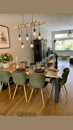 a dining room table with green chairs and lights hanging from it's ceiling above