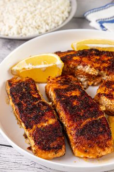 some fish and lemons on a white plate with rice in the backround