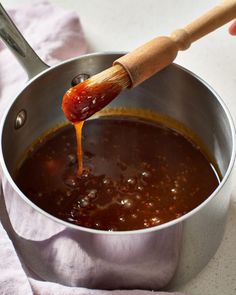 a wooden spoon pouring sauce into a pot