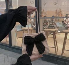 a hand holding a small purse with a bow on the front and side, in front of a store window