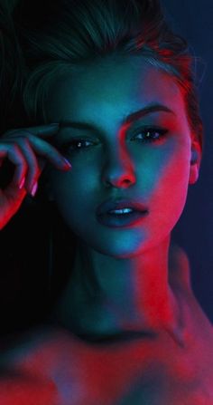 a beautiful young woman posing with her hand on her head and wearing red light makeup