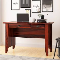 a desk with a laptop on it in front of some framed pictures and a chair