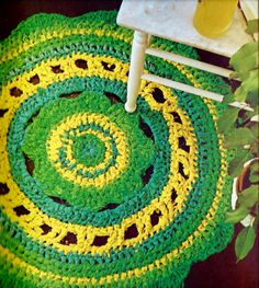 a green and yellow crocheted rug sitting on top of a wooden floor next to a white chair