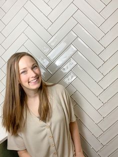 a woman standing in front of a white tiled wall with a smile on her face