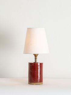 a red table lamp with a white shade on the base and a gold trim around it