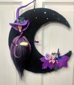 a purple and black witch wreath hanging on the front door with a doll in it