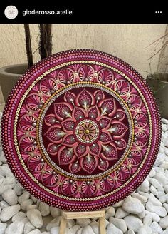 a red and gold decorative plate sitting on top of white rocks next to a potted plant