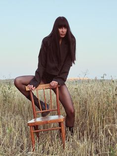 a woman sitting on top of a wooden chair in a field