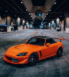 an orange sports car is parked in the middle of a parking garage with no one around it