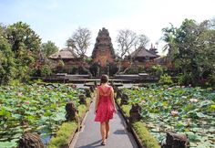 a woman in a red dress walking down a path next to water lilies and pagodas