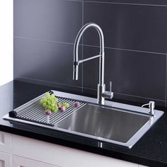 a stainless steel kitchen sink and faucet with black granite countertop in front of grey tile backsplash