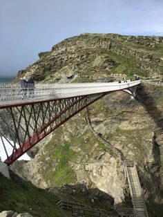 people walking across a bridge over the ocean on top of a cliff next to a body of water