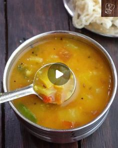 a ladle full of soup sitting on top of a wooden table next to a bowl of rice