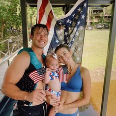 a man and woman holding a baby in front of an american flag