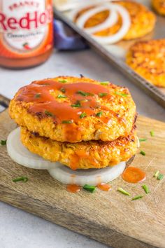 two chicken patties with ketchup and onions on a cutting board next to other food items