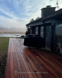 a wooden deck with an umbrella on it next to a house and water in the background