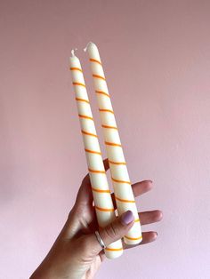 two orange and white striped candles are held in the palm of someone's hand