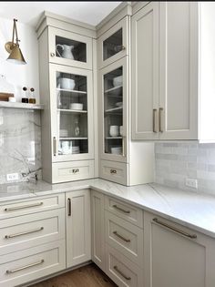 a kitchen with white cabinets and marble counter tops, gold pulls on the cupboards