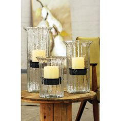 three glass vases with candles sitting on a wooden table next to a yellow chair