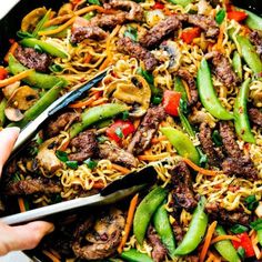 someone is cutting into some noodles with meat and veggies on top, in a skillet