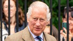 an older man wearing a suit and tie standing in front of a fence with people behind him