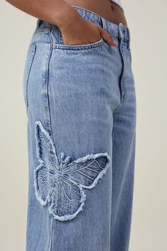 a woman wearing blue jeans with a butterfly applique on the back of her pants