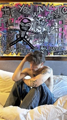 a man sitting on top of a bed in front of a large wall art piece