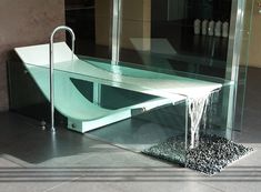 a bathtub that is sitting on the floor in front of a glass wall with water running down it