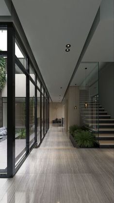 a long hallway with glass walls and stairs leading up to the second floor, along with potted plants on either side