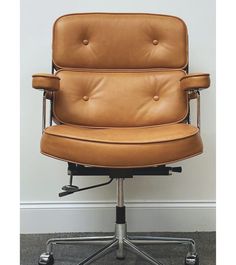 a brown leather office chair sitting in front of a white wall