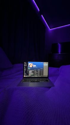 a laptop computer sitting on top of a bed in a room with purple lighting above it