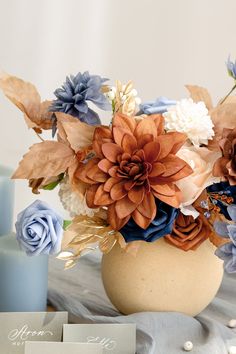 an arrangement of flowers in a vase on a table with two blue candles and some cards