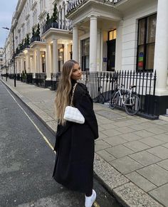 a woman is standing on the sidewalk in front of some buildings