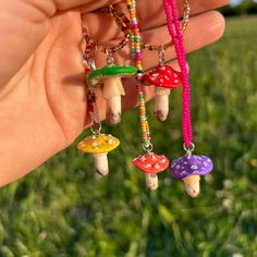 a hand holding three different colored beads with mushrooms hanging from it's end,