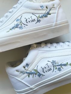 two white shoes with blue flowers painted on the side and one has an embroidered design