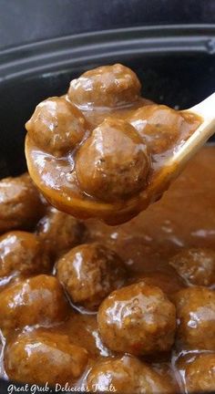 a ladle full of meatballs and gravy being held by a wooden spoon