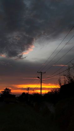 the sun is setting behind power lines and telephone poles in an area with green grass