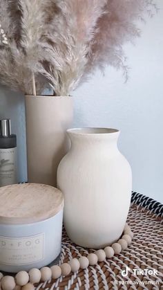 a white vase sitting on top of a table next to a container with some feathers in it