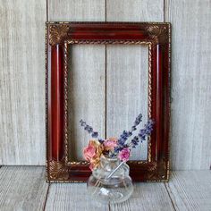 a vase with flowers in it sitting next to a wooden frame on a table top